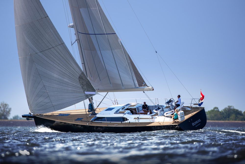 A blue-hulled yacht with a light wood deck under sail in the sunshine