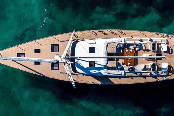 A bird's eye view of a sailing yacht with sails furled and people sitting one the light wooden deck