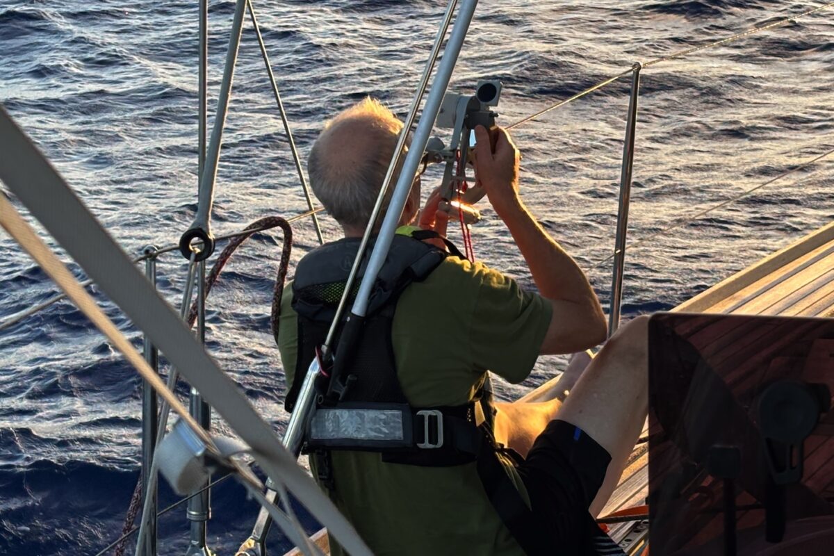 Man seated on side of sailing yacht using a sexton