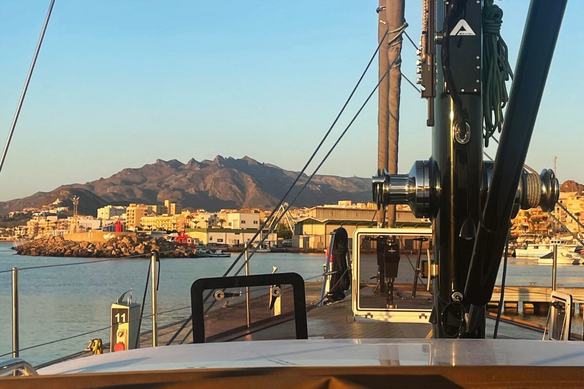 View from the stern of a sailing yacht looking forwards over the bow with village and mountains 